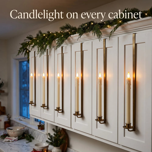Row of LED taper candles glowing on white kitchen cabinets with Christmas garland